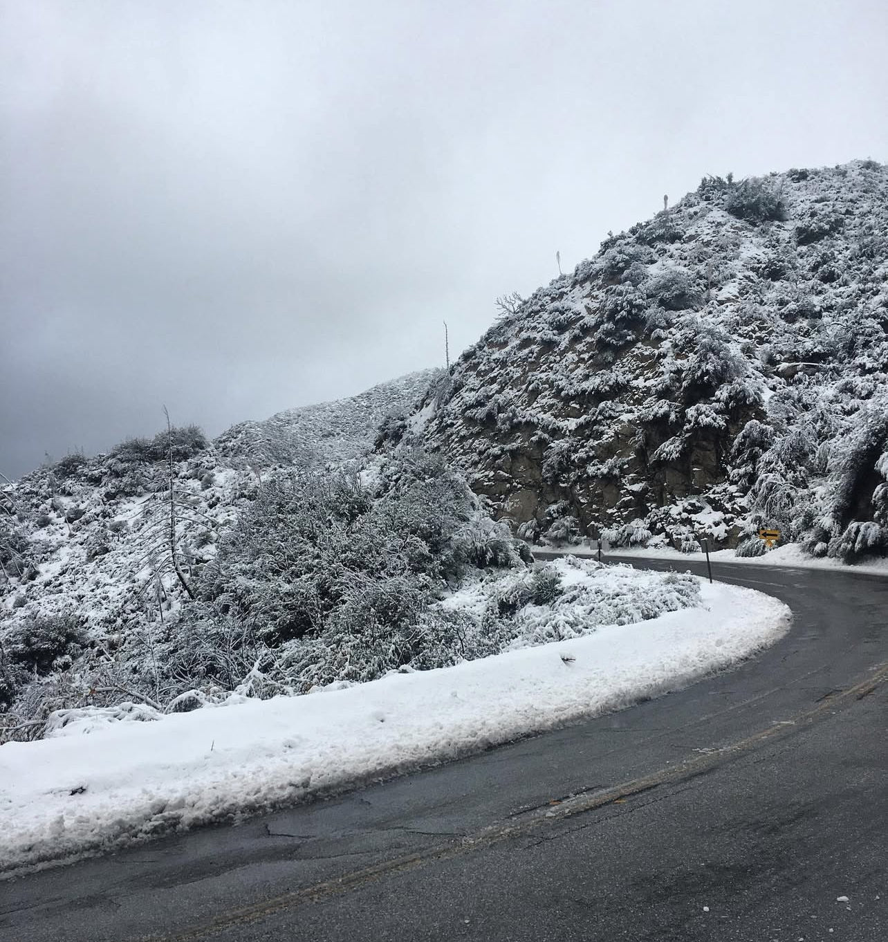 Winding road with snow-covered landscape and mountains under a cloudy sky